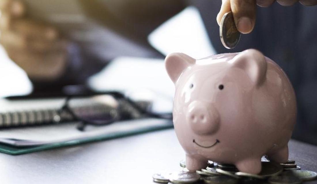 Sparschwein steht auf Münzen vor Notizblock und Taschenrechner