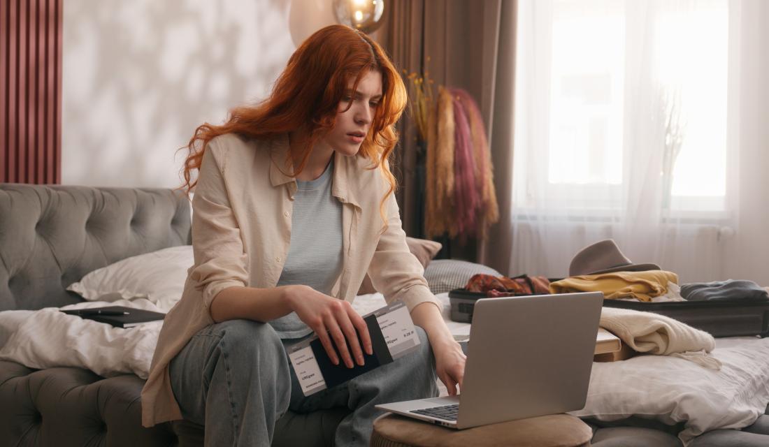 Schmuckbild: Frau, die gestresst auf Laptopbildschirm schaut und Reisepass und Flugtickets in der Hand hält.