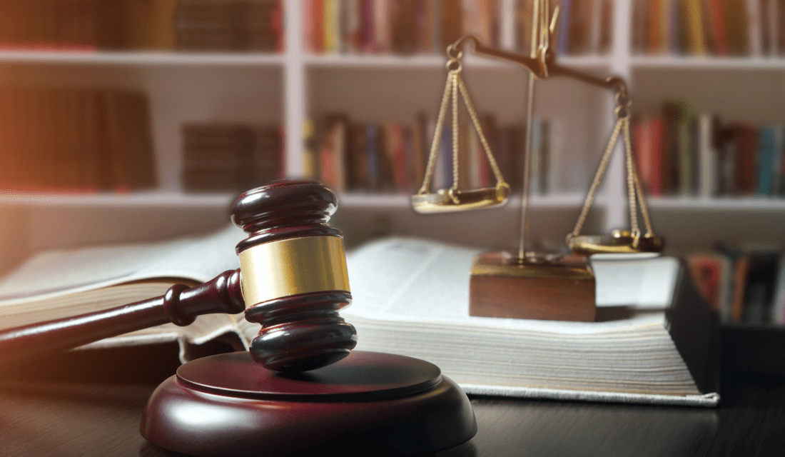 Eine Richterhammer liegt mit einem Gesetzbuch und einer Waagschale auf einem Tisch