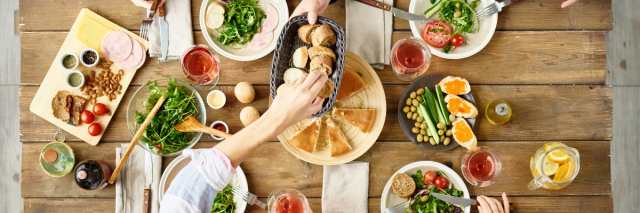 Blick von oben auf einen Holztisch mit Essen, Menschen essen gemeinsam