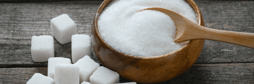 Auf einem Tisch sind Zuckerwürfel neben einer Schale mit Zucker gestapelt.