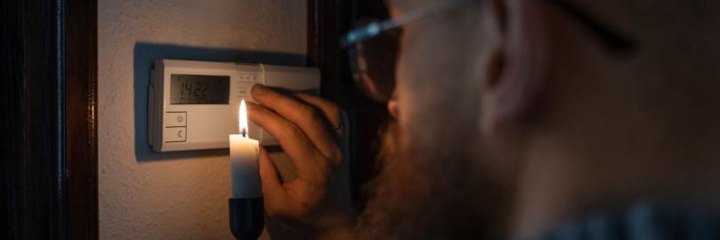 Ein Mann leuchtet bei Stromausfall mit einer Kerze am Sicherungskasten