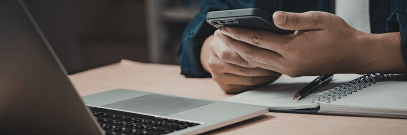 Person mit Handy in der Hand sitzt vor einem Laptop