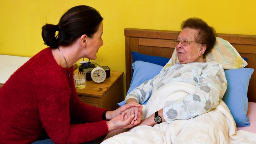 Eine Frau sitzt neben einer älteren Frau am Bett und hält ihre Hand