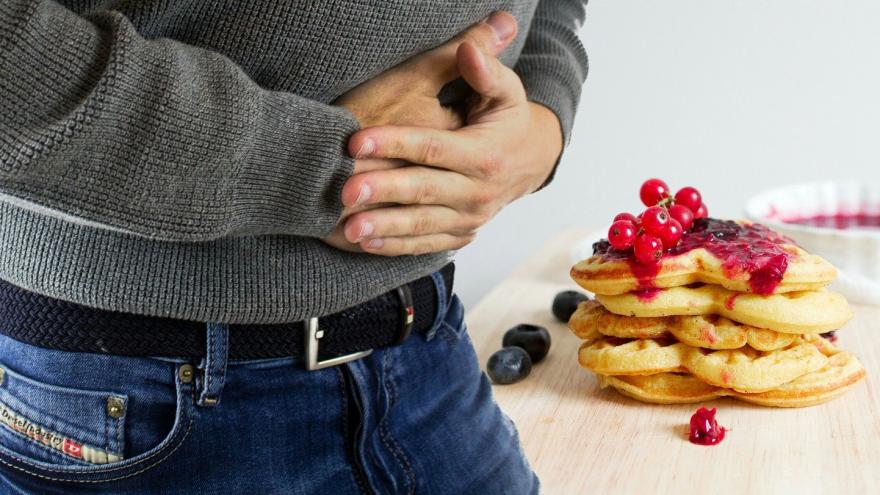 Mann hält sich den Bauch, im Hintergrund ist ein Teller mit Waffeln zu sehen