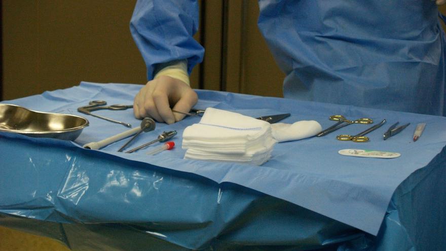 chirurgische Instrumente auf einem OP-Tisch, Hand des Chirurgen greift nach Material