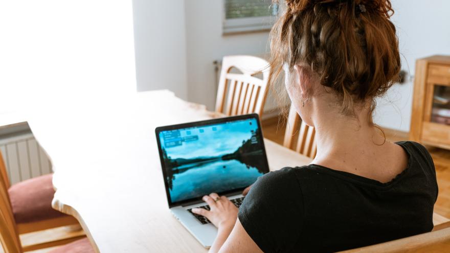 junge Frau, Rückansicht, sitzt am Esstisch vor einem Laptop