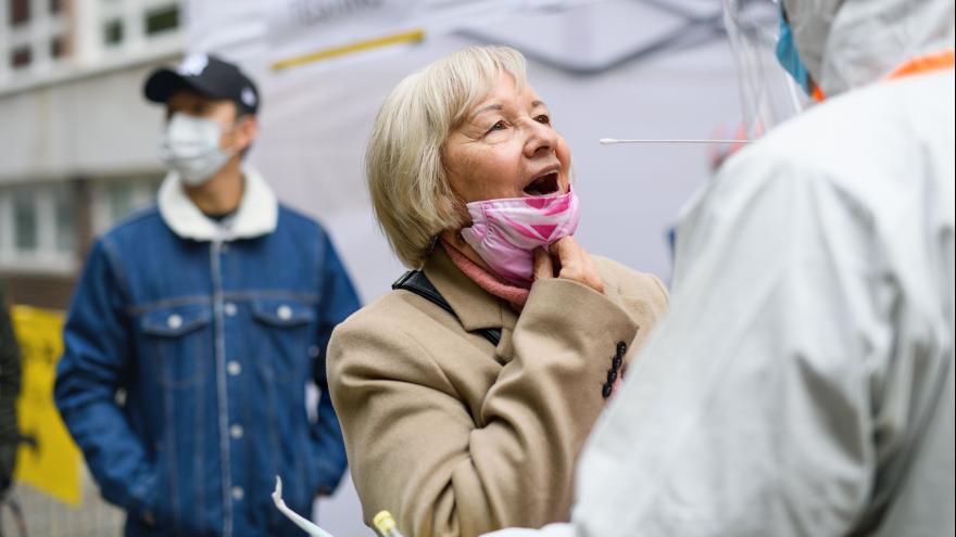 fröhlich aussehende ältere Frau wird mit einem langen Wattestäbchen auf das Coronavirus getestet