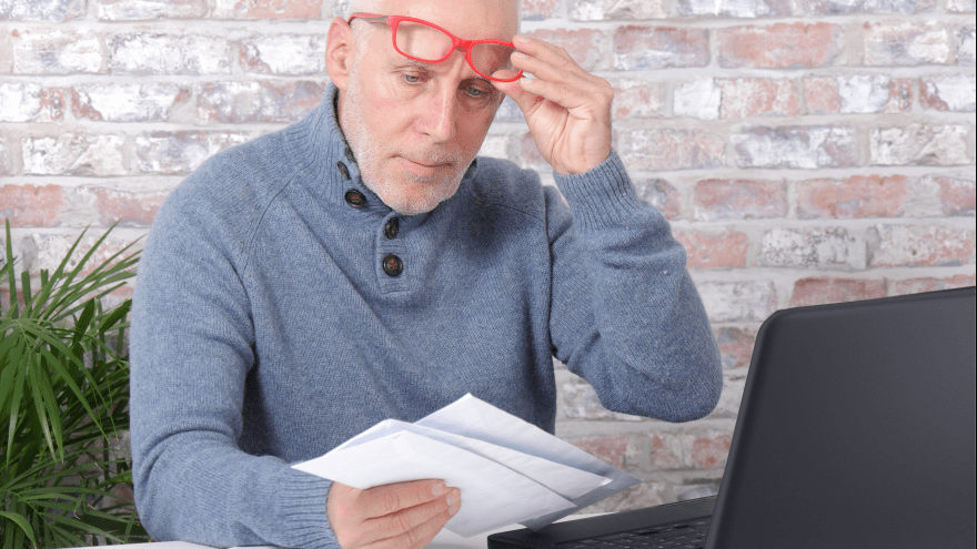 älterer Mann mit roter Brille öffnet Briefe mit ernster Miene