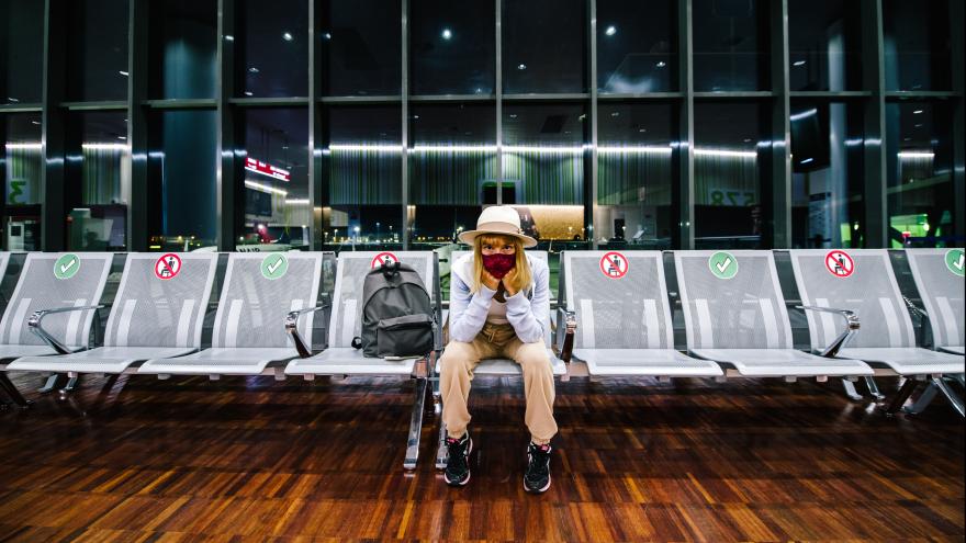Frau mit Gesichtsmaske sitzt alleine im Flughafen