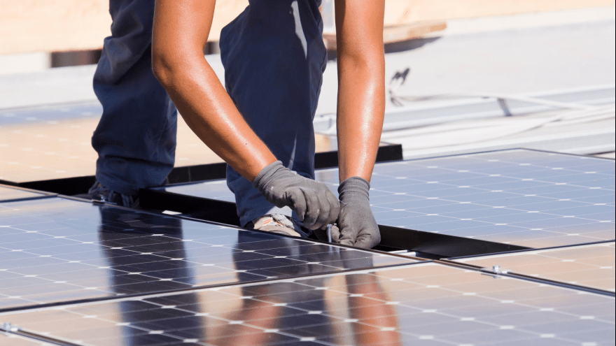 spiegelnde Photovoltaikmodule in Nahaufnahme, ein Handwerker mit Handschuhen arbeitet daran.