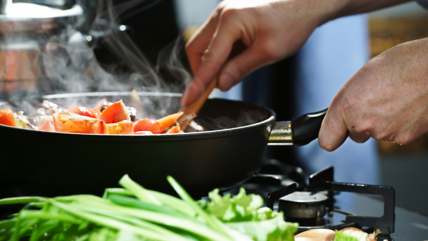 Pfanne mit dampfendem Gemüse, Hand hält Kochlöffel, Nahaufnahme