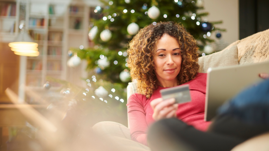 junge Frau auf dem Sofa mit Laptop und Kreditkarte, im Hintergrund ein Weihnachtsbaum