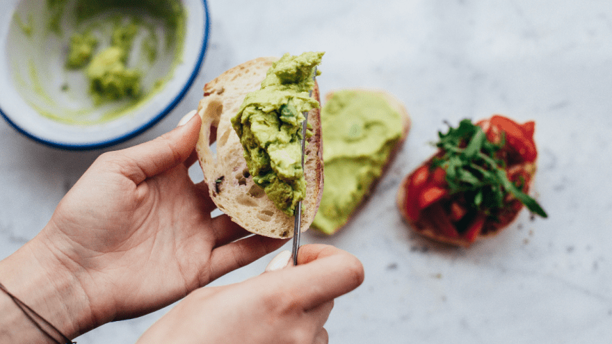 Frauenhände bestreichen ein Stück Ciabatta mit grüner Creme