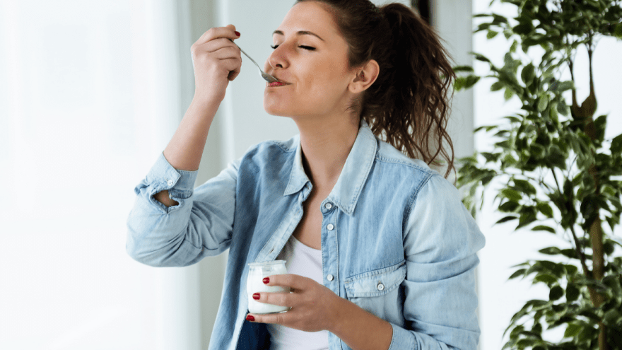 junge Frau löffelt genüsslich einen Joghurt aus einem Plastikbecher