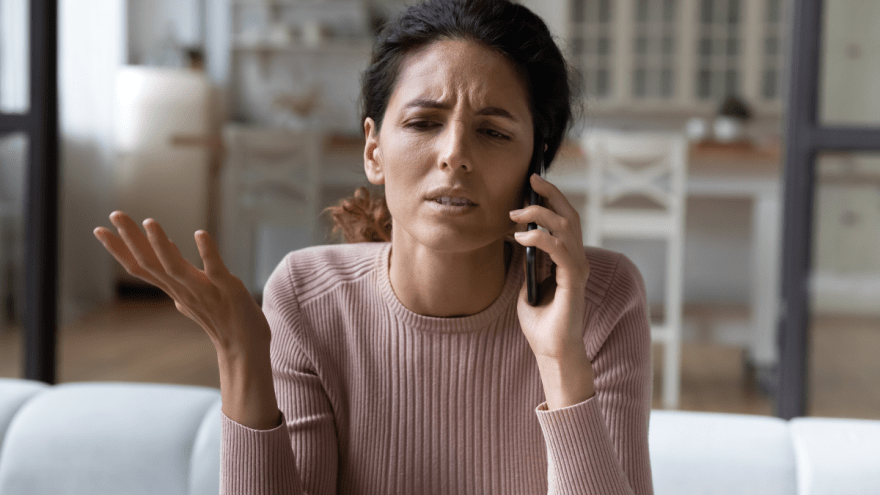 junge Frau mit dunklem Haar telefoniert mit verärgertem Gesicht