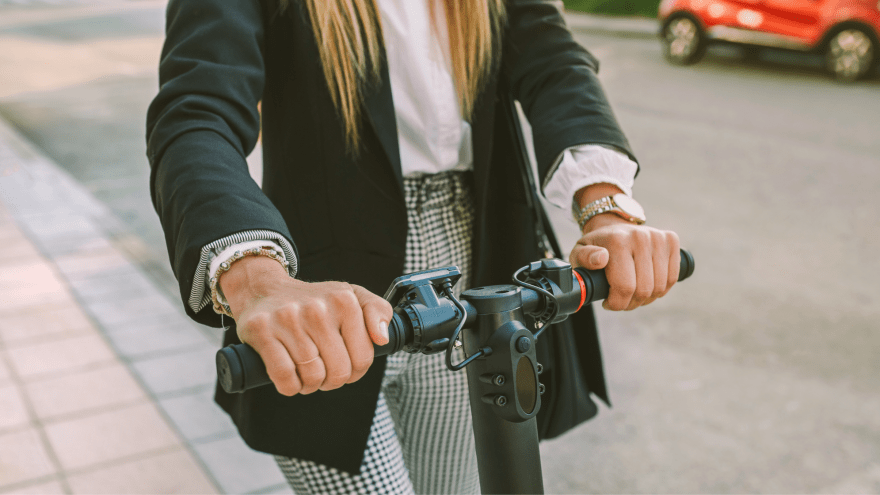 eine junge Frau fährt mit einem E-Scooter über einen Gehweg