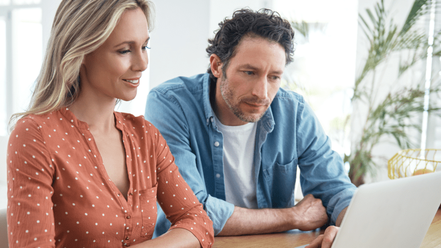 Eine Frau und ein Mann sitzen an einem Tisch und schauen auf einen Laptop