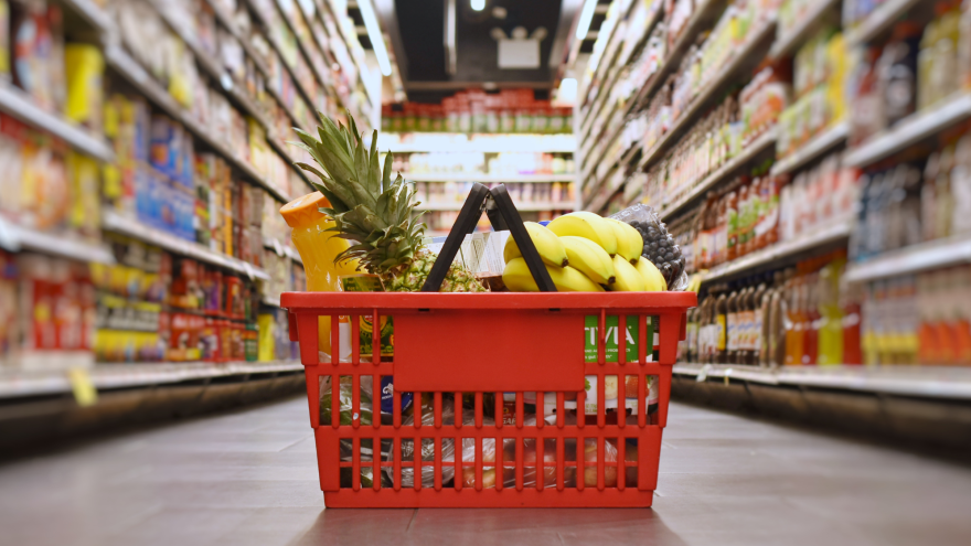 Ein gefüllter Einkaufskorb steht im Gang eines Supermarktes. 