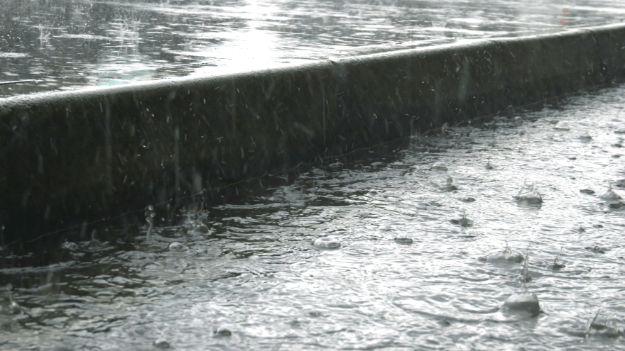 starker Regen fällt auf einen Gehweg, vor dem Bordstein sammelt sich das Wasser