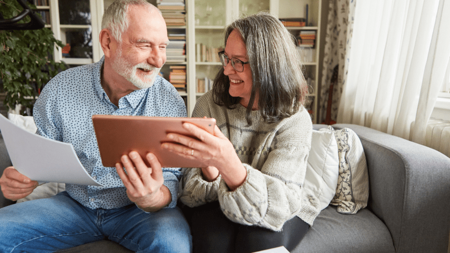 zwei ältere Menschen sitzen auf dem Sofa und haben ein Tablet in der Hand