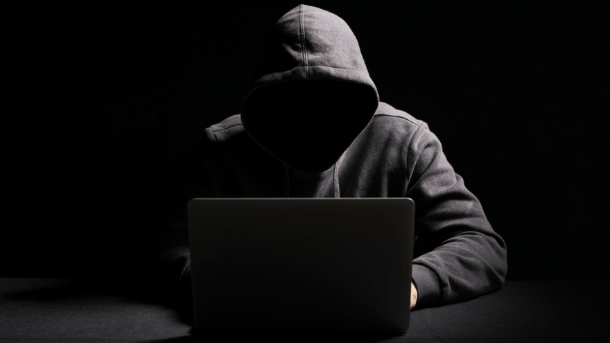 vermummte Person sitzt vor einem Laptop