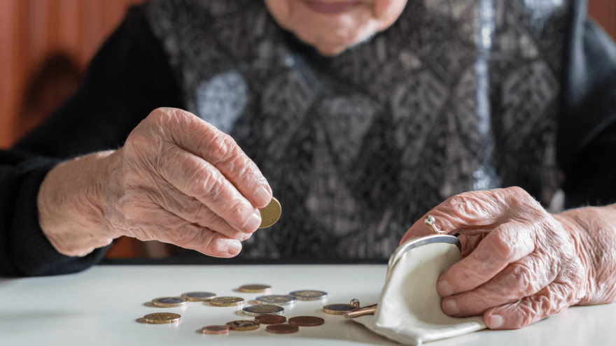 Eine ältere Dame zählt Bargeld, das vor ihr auf dem Tisch liegt