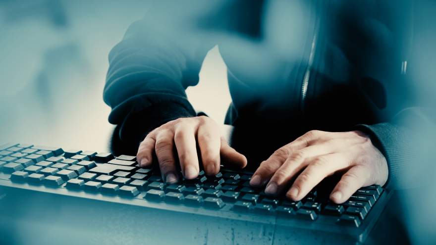 Ein in einem dunklen Hoody gekleideter Mensch tippt in eine Tastatur