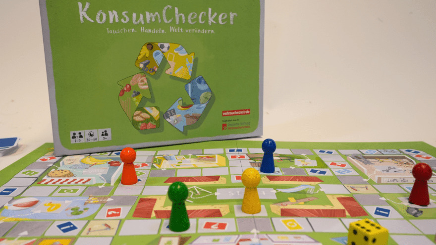 Brettspiel KonsumChecker aufgebaut mit Cover im Hintergrund