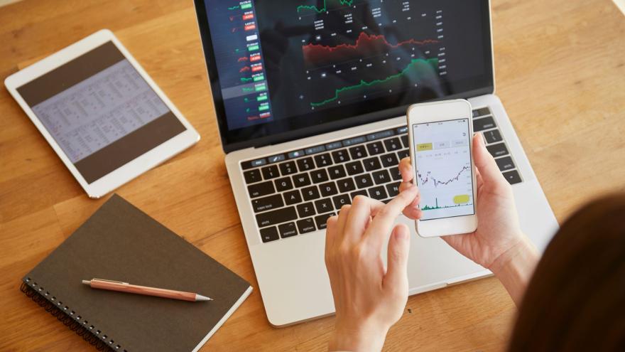 Jemand schaut sich Aktienkurse auf dem Laptop und dem Handy an