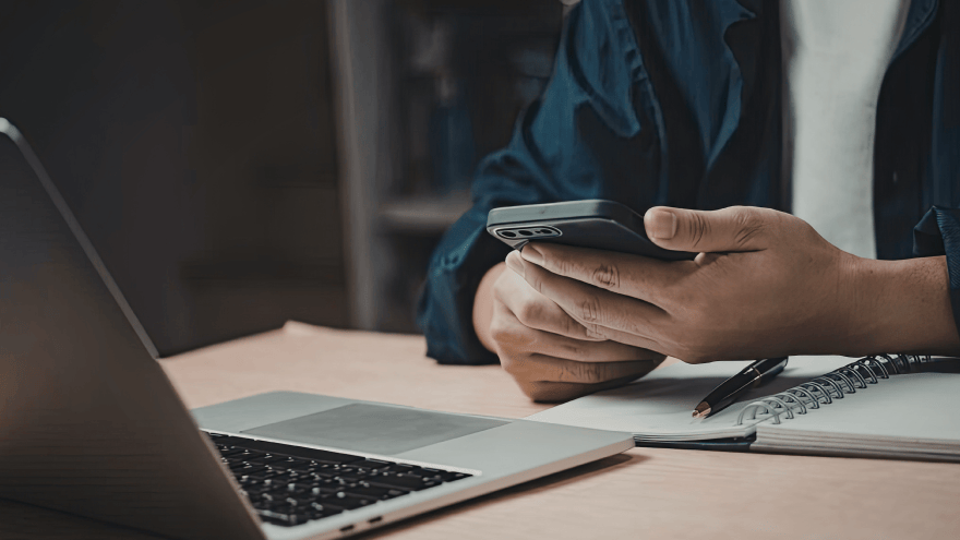 Person mit Handy in der Hand sitzt vor einem Laptop