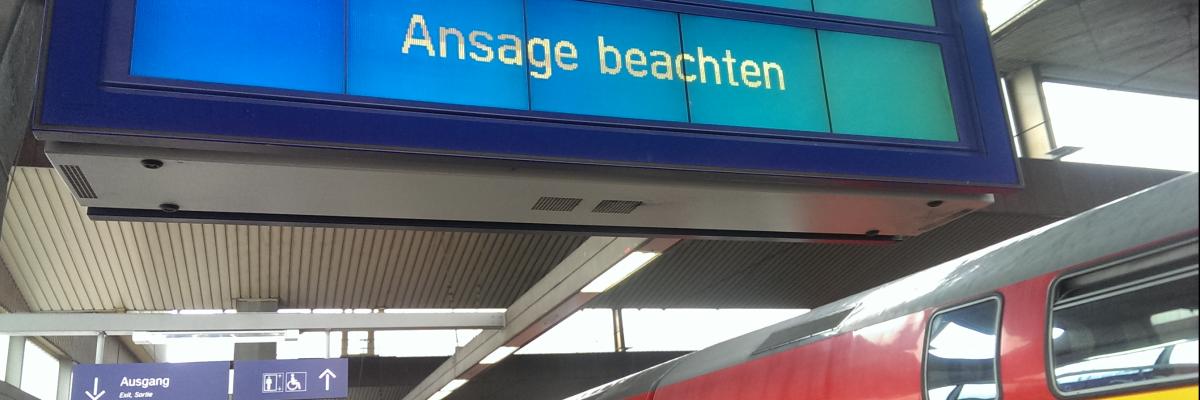 Ein doppelstöckiger Regionalzug steht an einem Bahnhofsgleis, auf der Anzeige steht: "Ansage beachten"