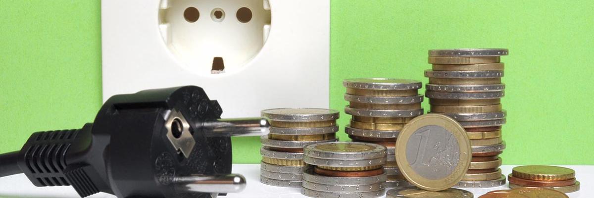 Stromstecker und Münzen liegen vor einer Steckdose