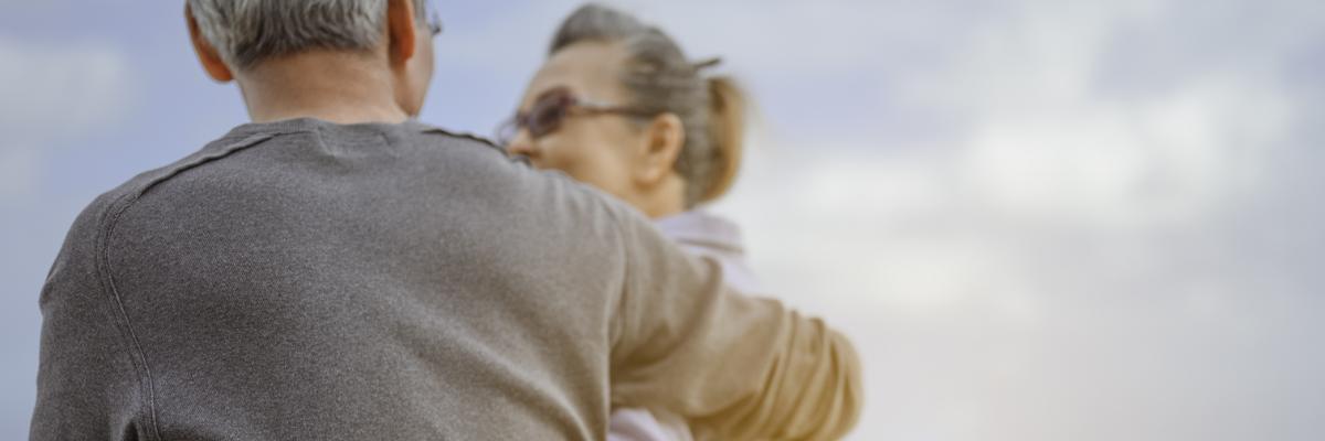 Ein älteres Paar sitzt gemeinsam am Strand und hält sich im Arm.