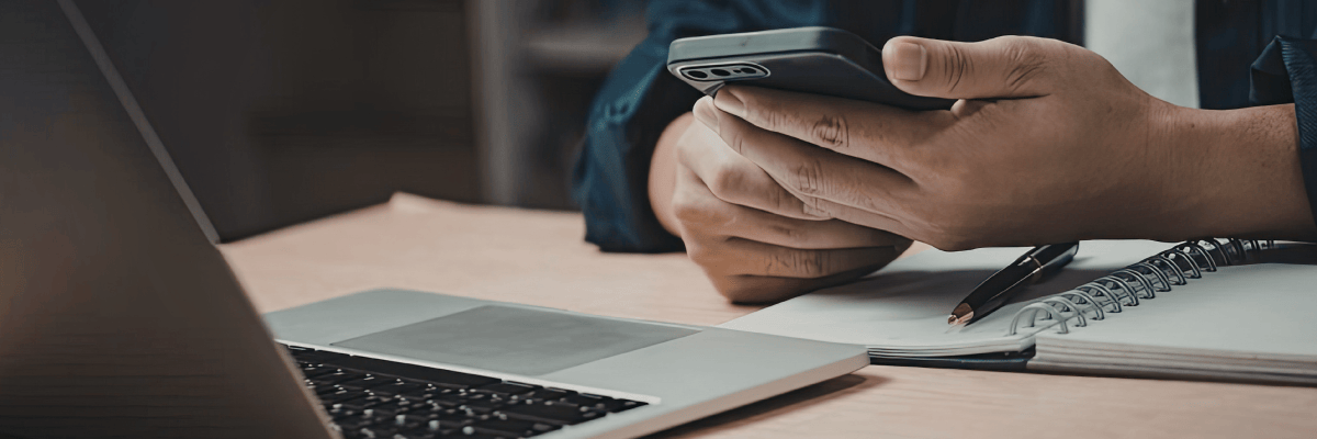 Person mit Handy in der Hand sitzt vor einem Laptop