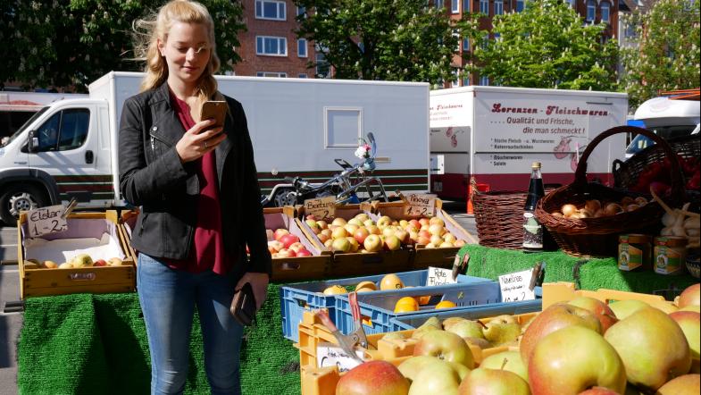 Junge Frau mit Smartphone auf dem Wochenmarkt