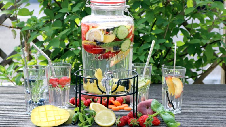 Großer Behälter mit Wasser, Früchten und Gemüse gefüllt, darum Gläser, Früchte und Gemüse.