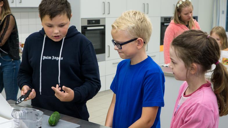 drei Kinder in der Schulküche beim Gemüseschneiden