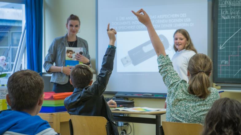 Blick in eine Schulklasse mit Lehrerin, Schüler melden sich per Handzeichen