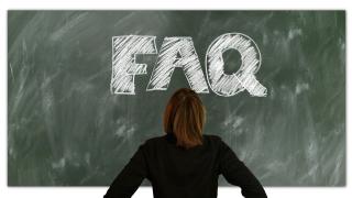 Eine Frau steht vor einer Tafel, auf der mit Kreide "FAQ" geschrieben wurde.