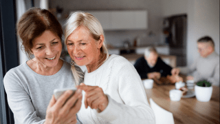 Zwei sportlich wirkende Frauen um die 70 schauen in der Küche gemeinsam auf ein Smartphone