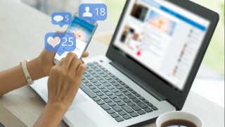 Hände einer jungen Frau halten ein Smartphone vor einem Laptop