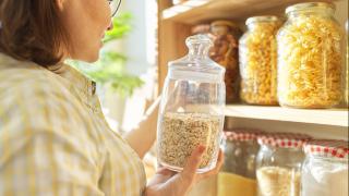 Frau nimmt ein Glas mit Haferflocken aus einem Vorratsregal mit vielen gefüllten Gläsern