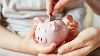 Jemand wirft eine Münze in ein Sparschwein.