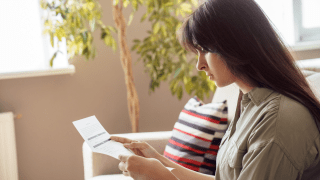 junge Frau mit dunklem Haar liest einen Vertrag, Hintergrund Wohnzimmer