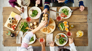 Blick von oben auf einen Holztisch mit Essen, Menschen essen gemeinsam