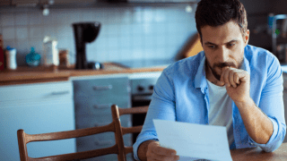junger Mann am Küchentisch schaut sorgenvoll auf einen Brief