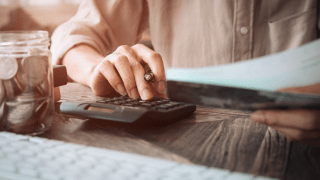 Nahaufnahme einer Person, die am Schreibtisch einen Taschenrechner bedient