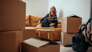 Eine junge Frau sitzt inmitten verschiedener Umzugskartons auf einem Sofa