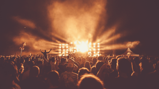 eine Menschenmenge blickt auf die Bühne, Scheinwerfer erleuchten die Menge 